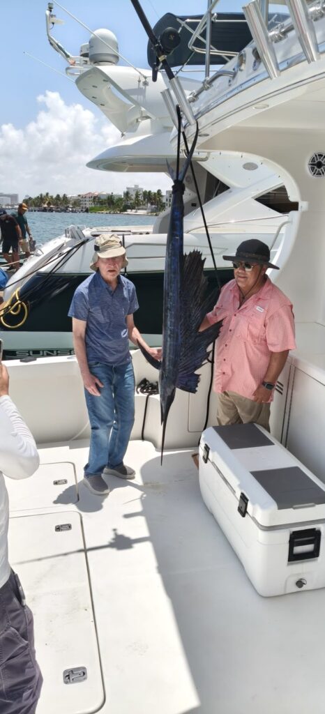 Clientes con un pez vela a bordo de un yate de pesca deportiva en Cancún